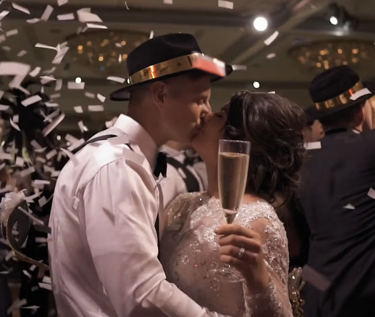 At a Rittenhouse Hotel wedding, a couple kisses while holding champagne glasses, surrounded by falling confetti.
